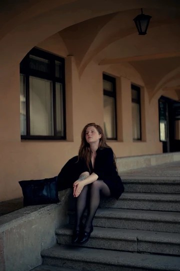 Portrait seated on stone steps beneath an arcade